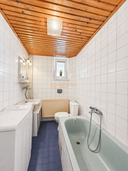 Bathroom with tiles, blue floor, bathtub, and wooden ceiling in a family house.