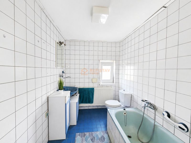 A bathroom with a shower and a bathtub tiled with white tiles in a family house.
