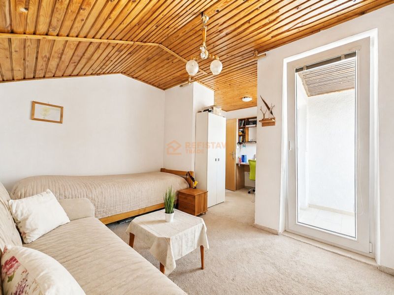 A room in a family house with a wooden ceiling, a sofa, and a workspace.