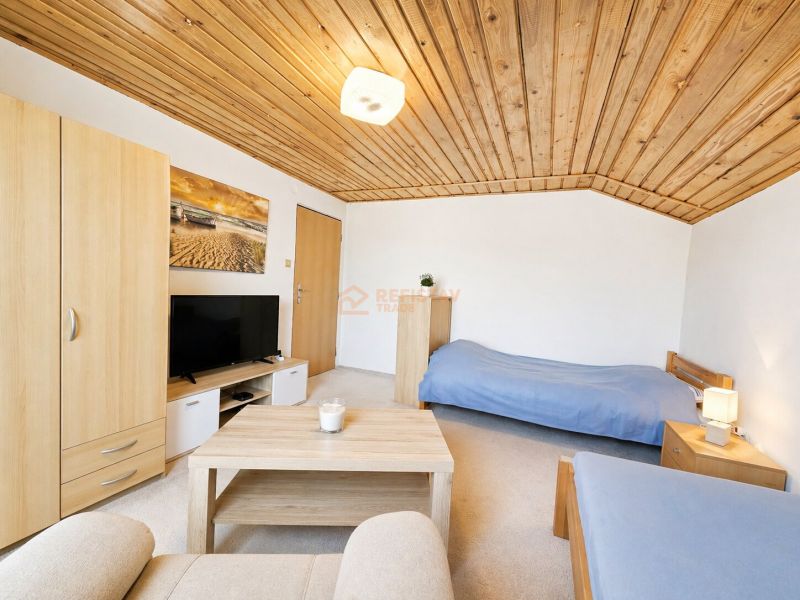 A room in a family house with a wooden ceiling, beds, and a TV.