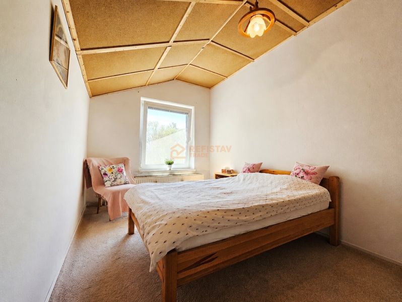 Bedroom in a family house with a wooden ceiling, carpet, and a bed with pillows.