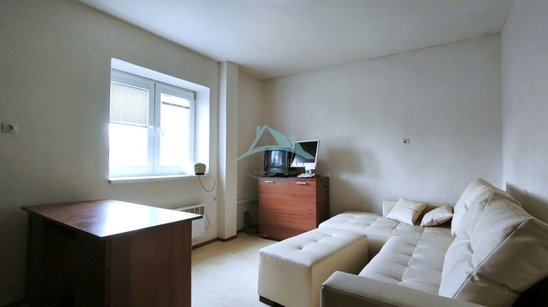 A room with a couch, table, wooden decor, TV, and a window with blinds.