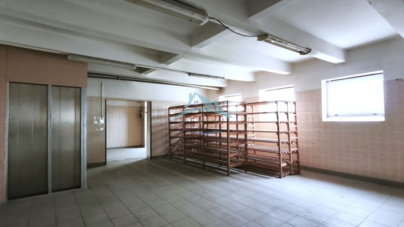 Production premises with shelves and an elevator, illuminated by windows, with ceramic flooring.