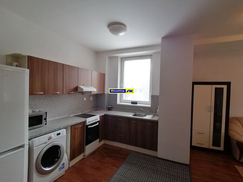 Kitchen of a 2-room apartment with a kitchen unit, washing machine, refrigerator, and floor with wooden decor.