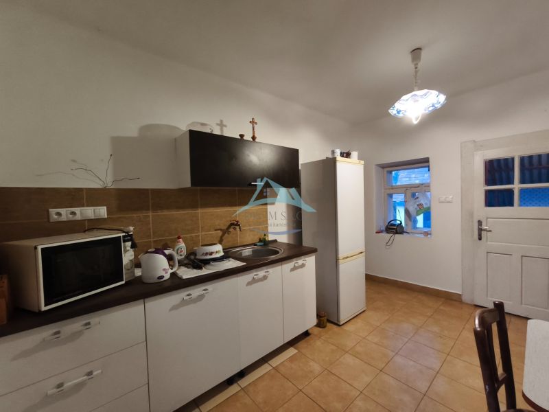 A kitchen in a family house with brown tiles, equipped with a microwave and a refrigerator.