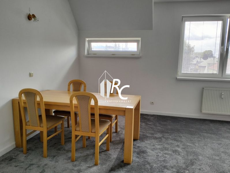 A table with four chairs in a two-room apartment, gray carpet, two windows.