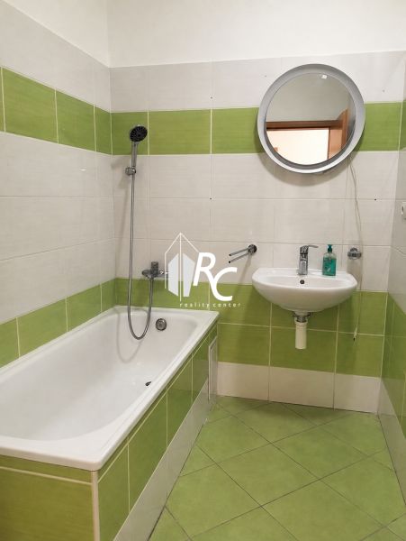 Bathroom in a 2-room apartment with emerald green tiles and a round mirror.