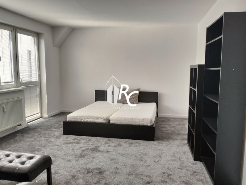 Bedroom in a 2-room apartment with a bed, shelves, and a carpet in neutral colors.