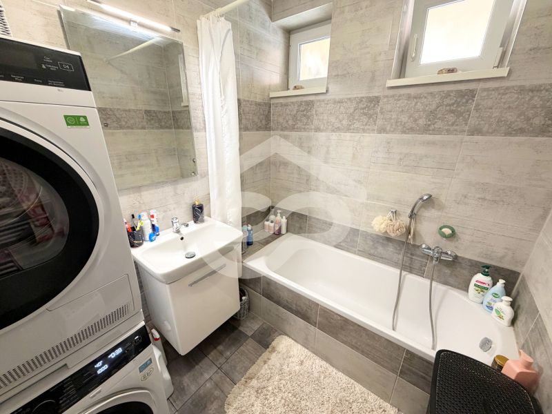 Bathroom in a family house with a bathtub, sink, and a washing machine with a dryer.