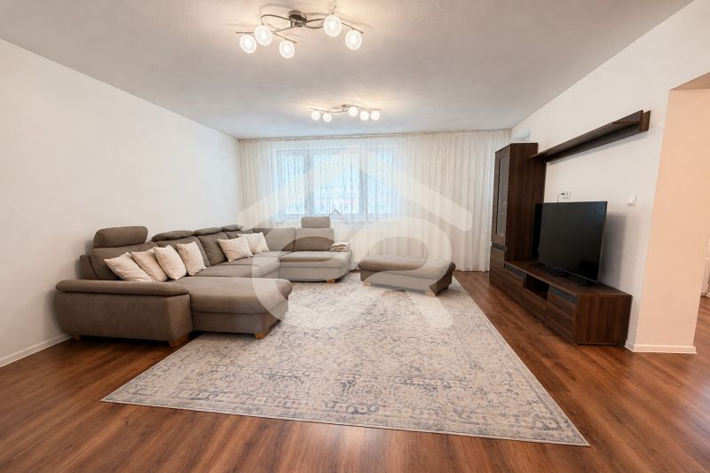 Living room with a large sofa, television, and wooden decor flooring in a family house.