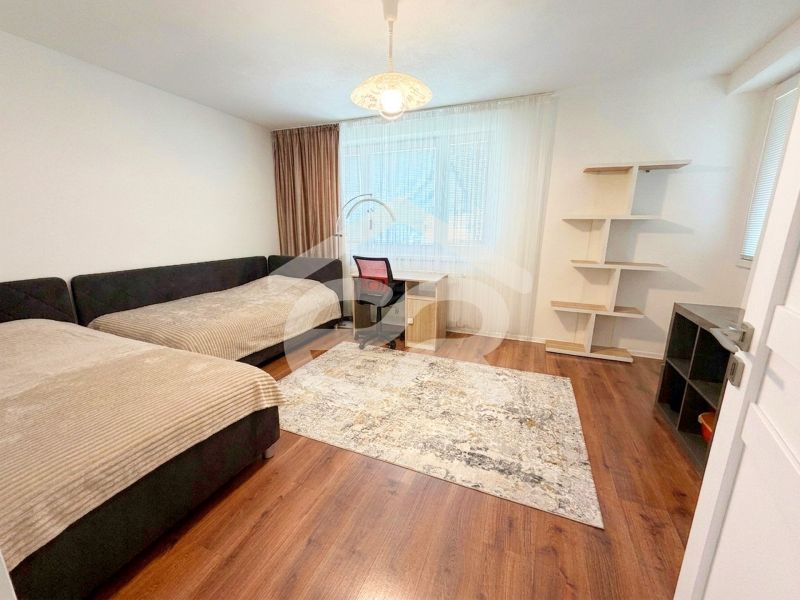 Two beds, a desk, and a shelf in a room of a family house with a wood-patterned floor.