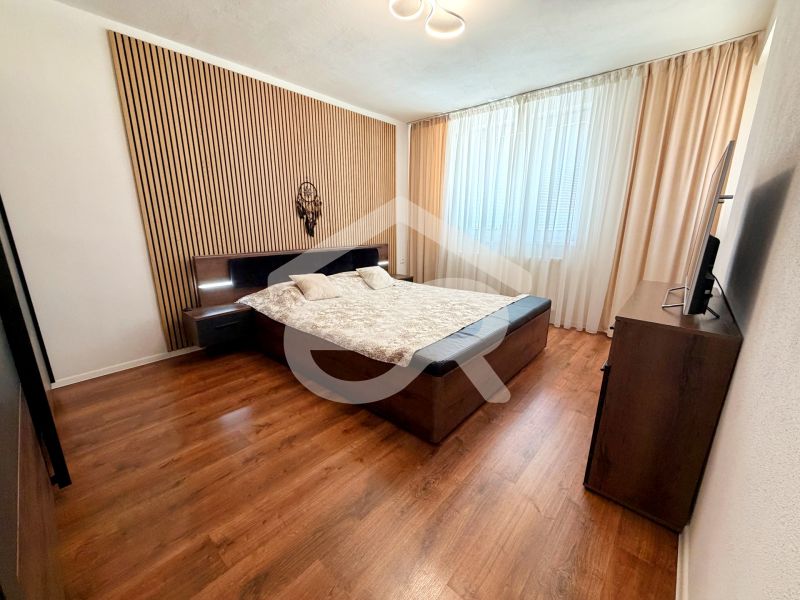 Bedroom in a family house with a bed, curtains, and a wood-patterned floor.