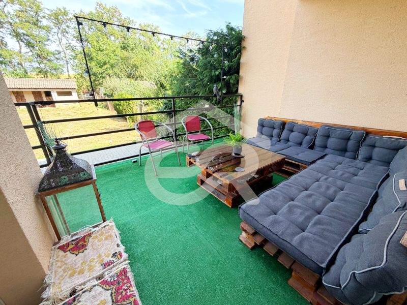A balcony of a family house with pallet seating, a green carpet, and a view of the garden.