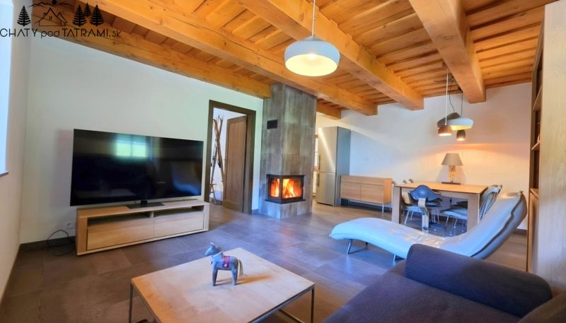 Living room in a cottage with a fireplace, television, and wooden ceilings.