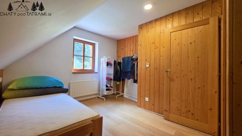Part of a bedroom in a cabin with a single bed, window, and coat rack, floor with wooden decor.