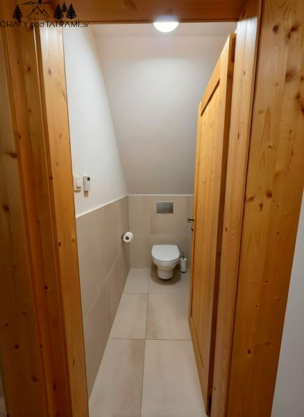 Interior of a cabin with a toilet, light tiles, and wooden paneling on the door walls.