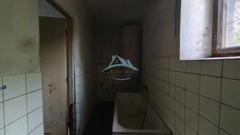 A bathroom with a bathtub and tiles in a family house. Damage is visible on the wall.