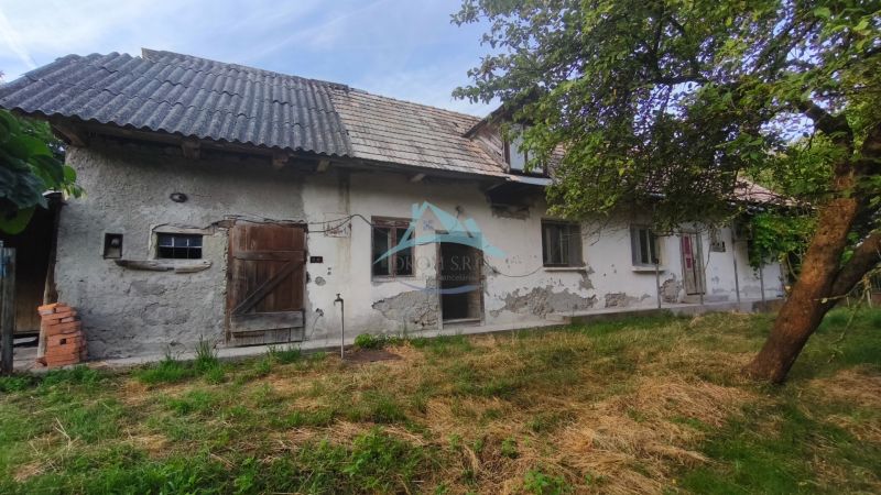 A family house in Čelovce with worn-out plaster, wooden doors, and a garden.