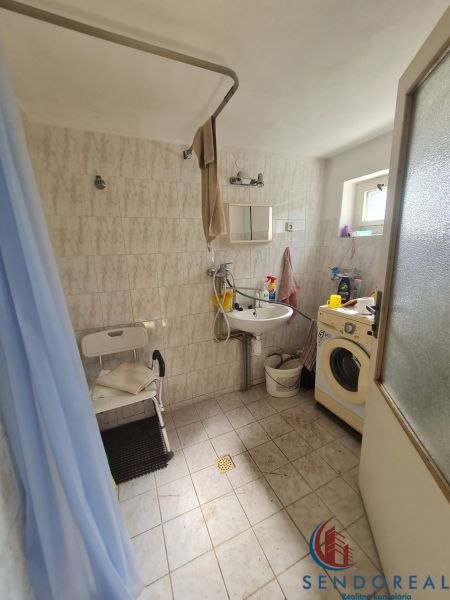 A bathroom in a family house with a washing machine, shower, and small window.