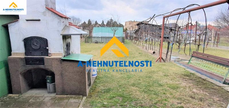 The yard of a family house in Veľký Meder with an outdoor fireplace and a gazebo on the grass.