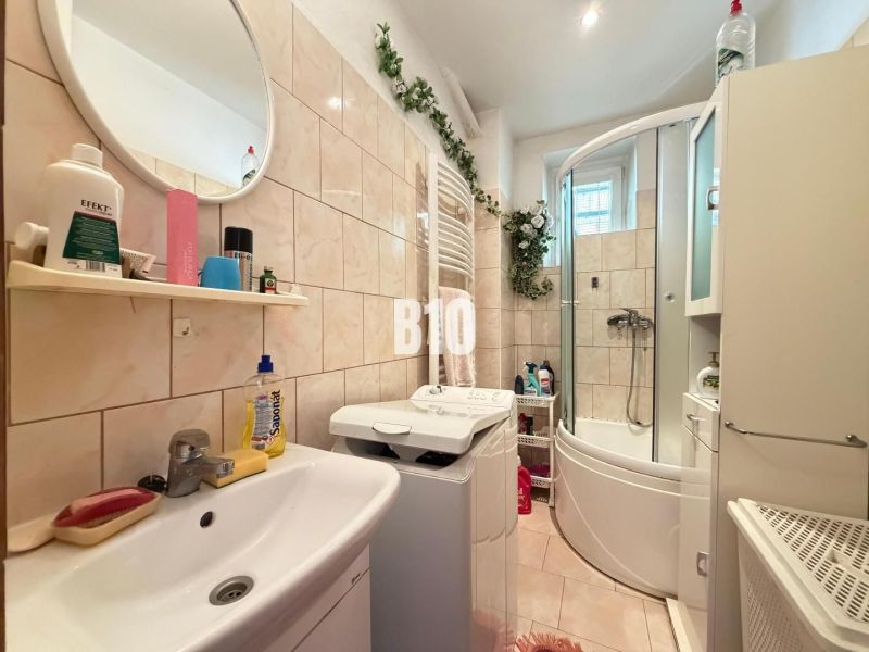 A bathroom in a family house with a washing machine, bathtub, sink, and a shelf with products.