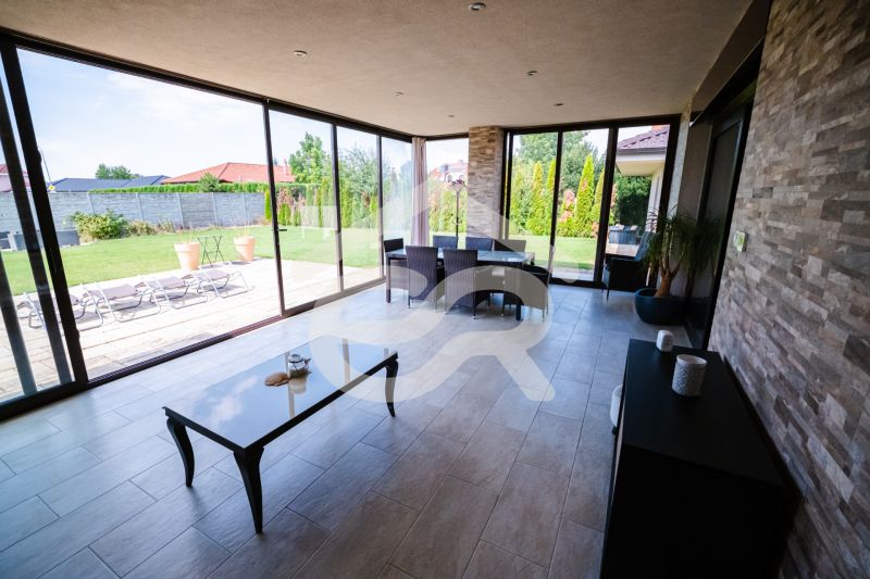 A glazed terrace of a family house with a view of the garden and a tiled floor.