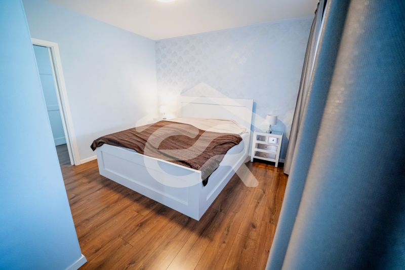 A bedroom in a family house with a bed, nightstands, and a floor with a wood decor.