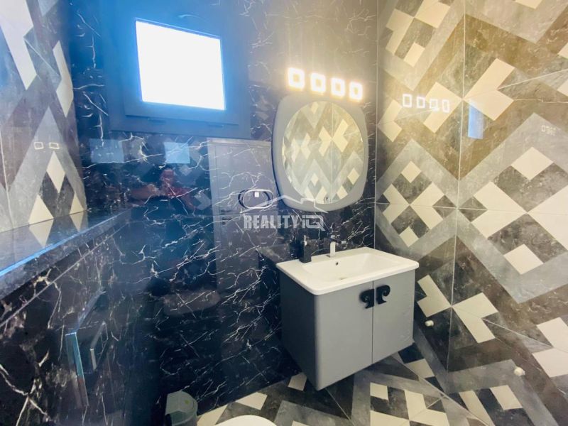 A bathroom in a family house with a sink, patterned tiles, and a window.