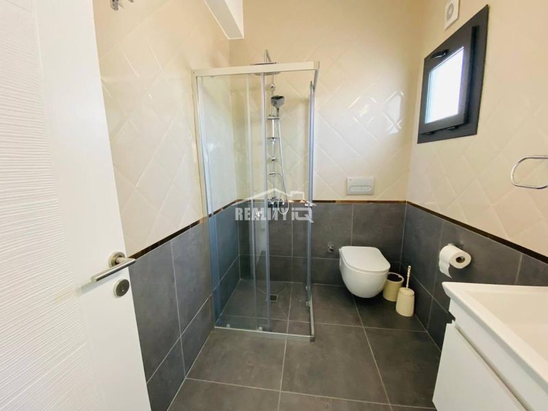 A bathroom in a family house with a shower, dark tiles, and light wall tiles.