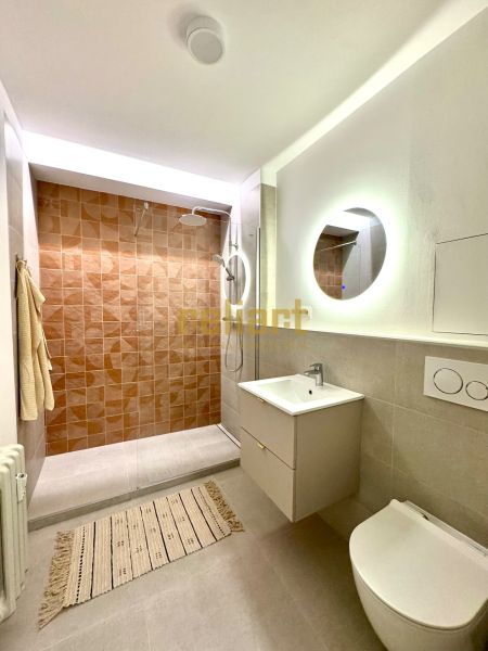 A bathroom in a studio apartment with a walk-in shower and a round mirror.