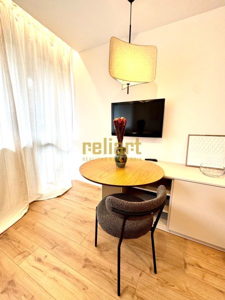 A table with a chair and a television in a studio apartment, floor with wood decor.