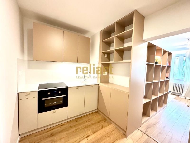 A kitchen unit with a cooktop and shelves in a studio apartment with a wood-patterned floor.