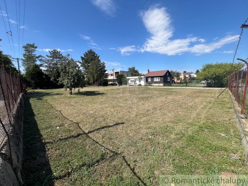 A flat plot of land in Bernolákovo with a grassy area surrounded by trees and fencing.