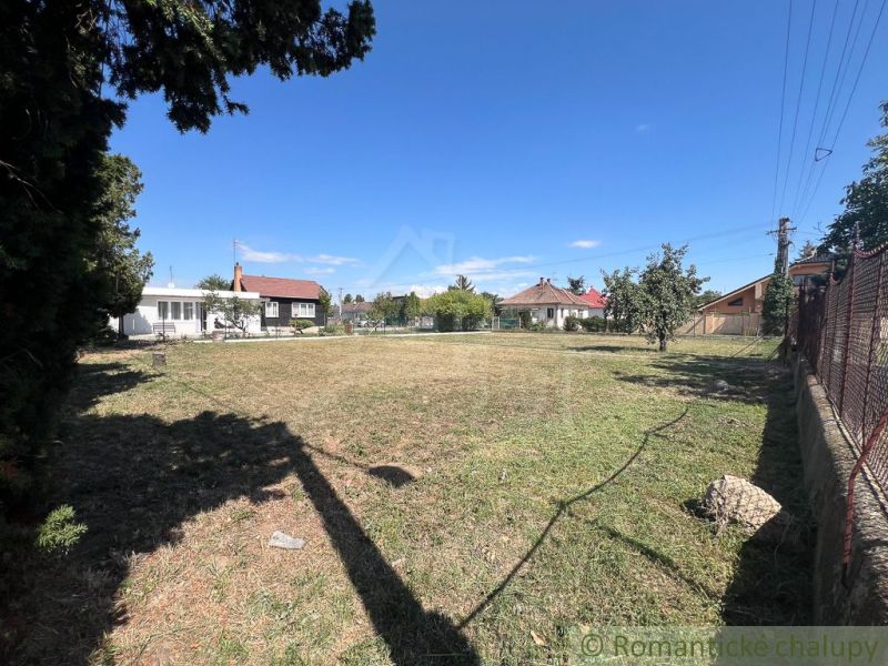 Gardens in Bernolákovo with a lawn, trees, and surrounding houses on a sunny day.