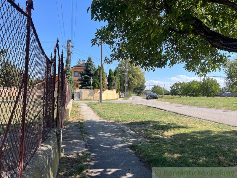The path runs alongside the fence in the gardens of Bernolákovo, with the road in the background.