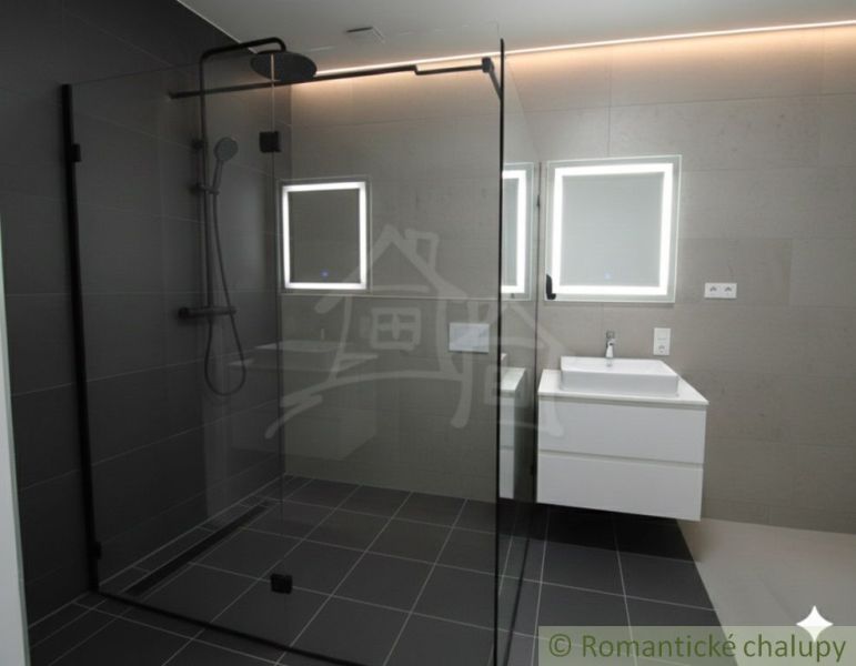 A bathroom in a family house with a glass shower enclosure and backlit mirrors.