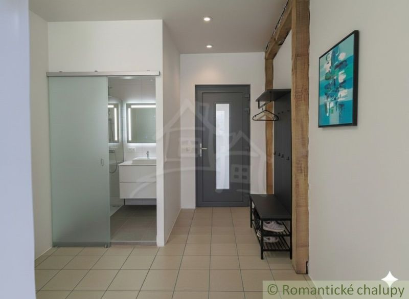 A hallway with ceramic tiles, glass doors, a sink, and a coat rack in a family house.