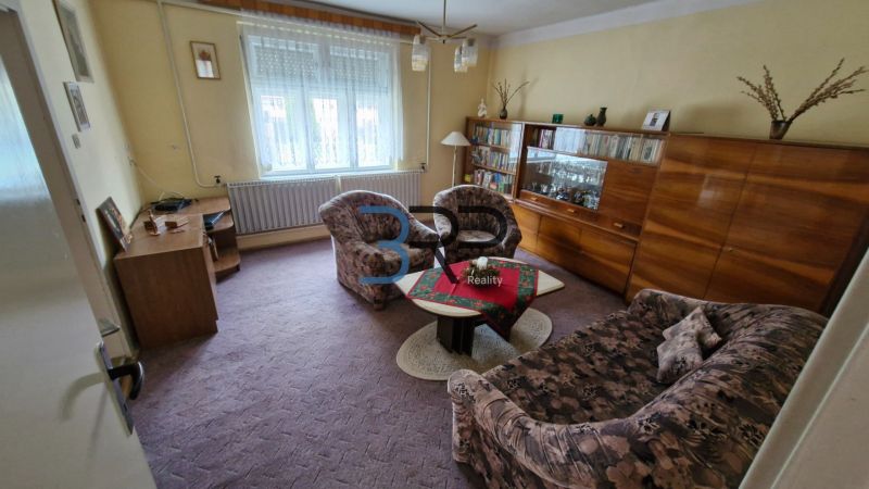 Living room in a family house with carpeted floor, furniture, and decorations on the shelves.