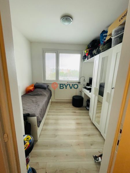 A small room in a 3-room apartment with a bed and a wardrobe, floor with wooden decor.