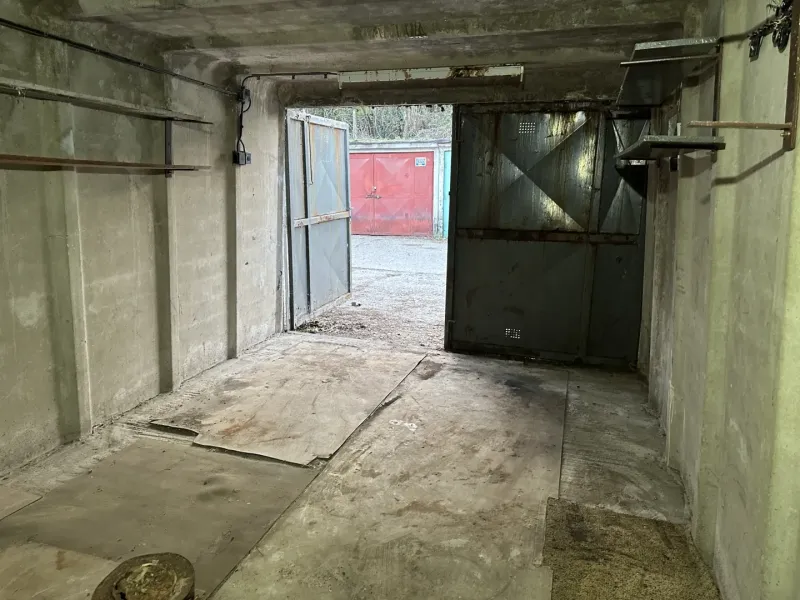 Concrete garage with open steel doors, view of another garage outside.