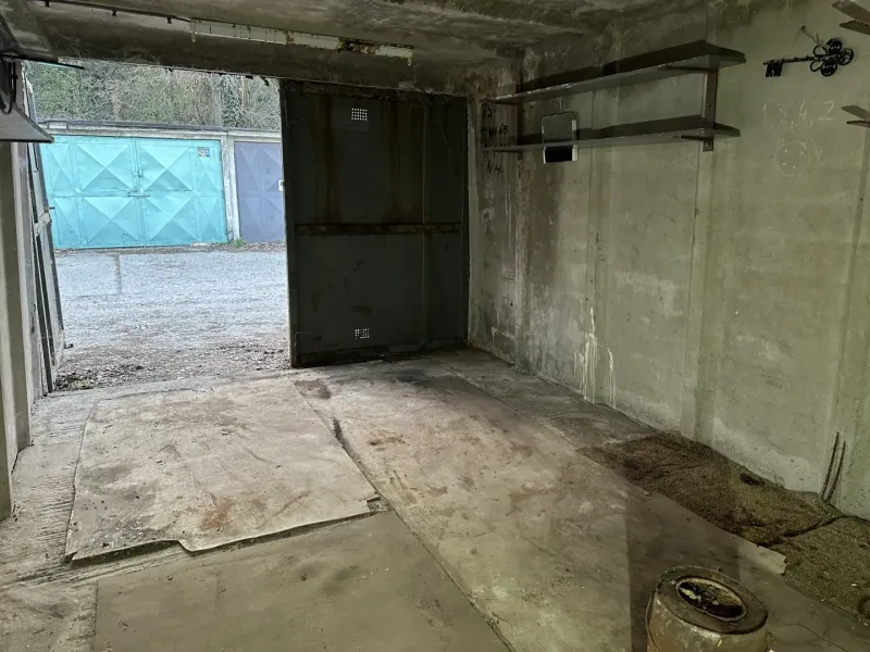 The interior of a garage with a concrete floor and metal shelves.