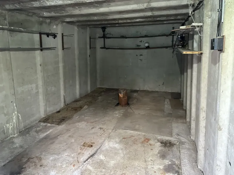 The interior of a garage with concrete walls and shelves for storage.
