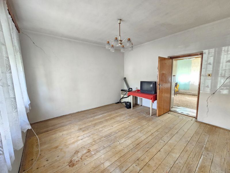 A room with a wooden decor floor in a family house, a table, and an older television.