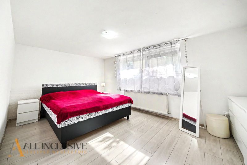 A bedroom in a family house with a red bed and a floor with a wood decor.