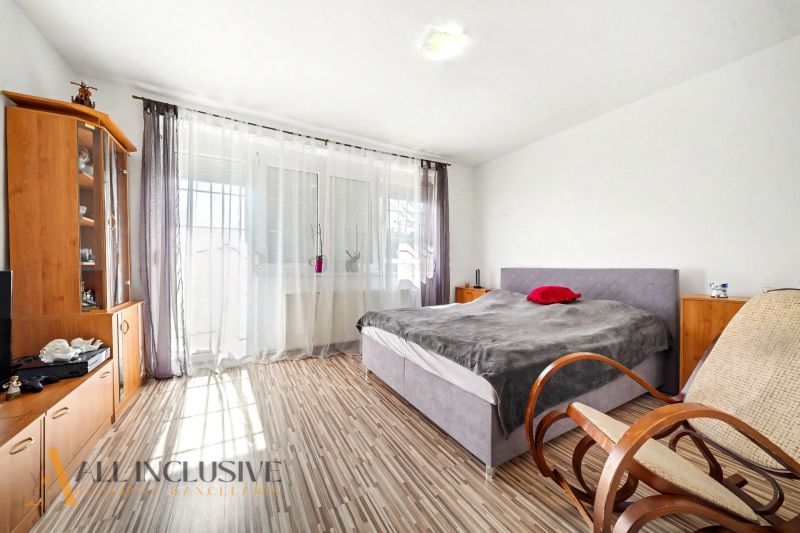 A bedroom in a family house with a wood-patterned floor, thoughtfully arranged furniture, and a rocking chair.