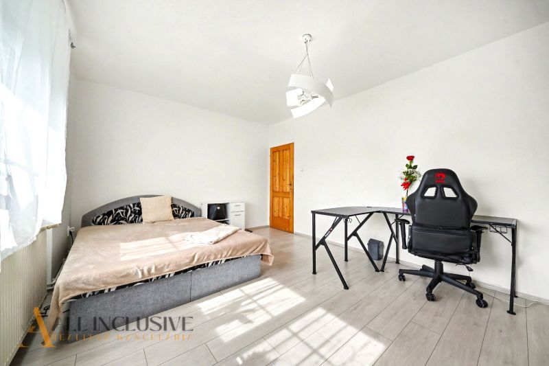 A room in a family house with a bed, table, and chair on a floor with a wooden decor.