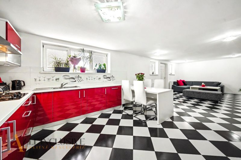Bright kitchen and dining room in a family house with black and white tiles and red cabinets.