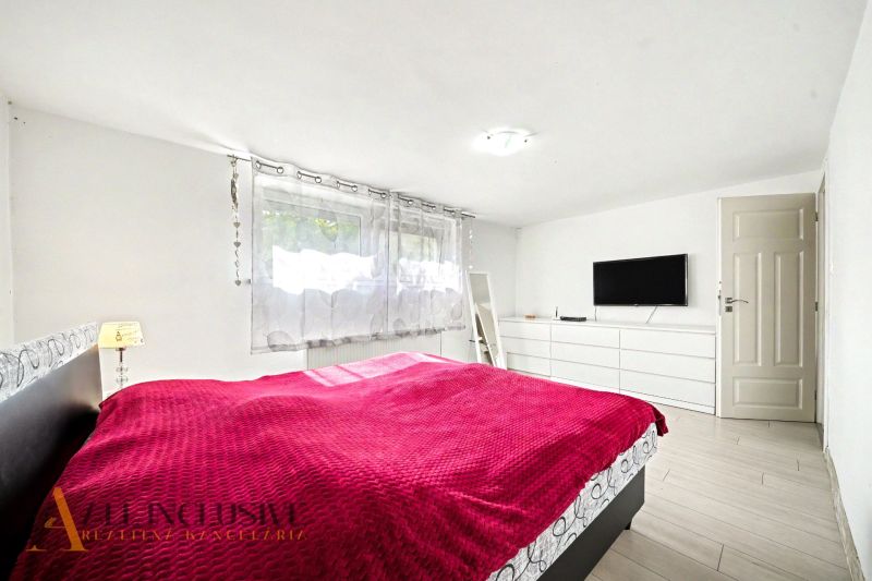 A bright bedroom with a red blanket, a TV on the wall, and a wooden decor floor.