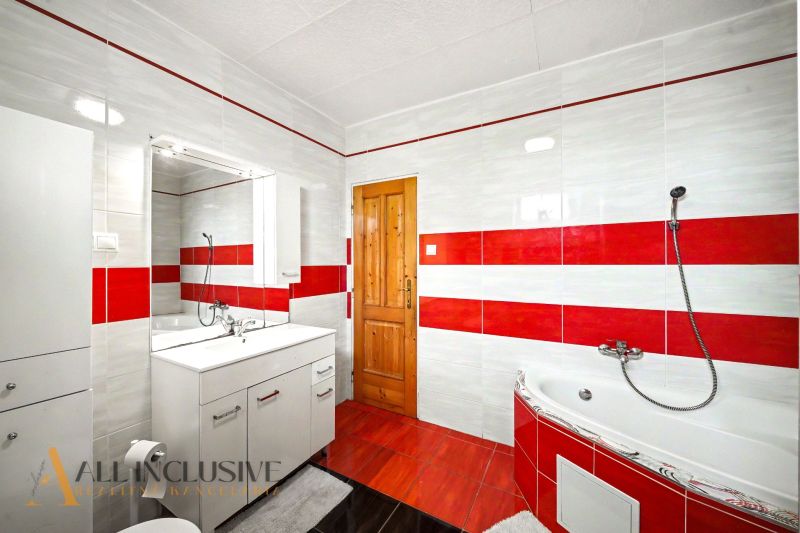 A family house bathroom with red and white tiles, a corner bathtub, and cabinets.