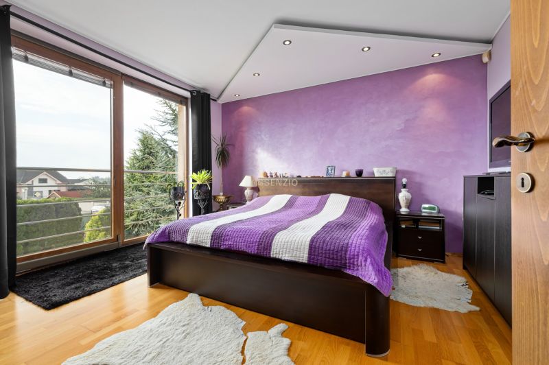 A bedroom in a family house with a purple wall, a bed, and a wooden decor floor.